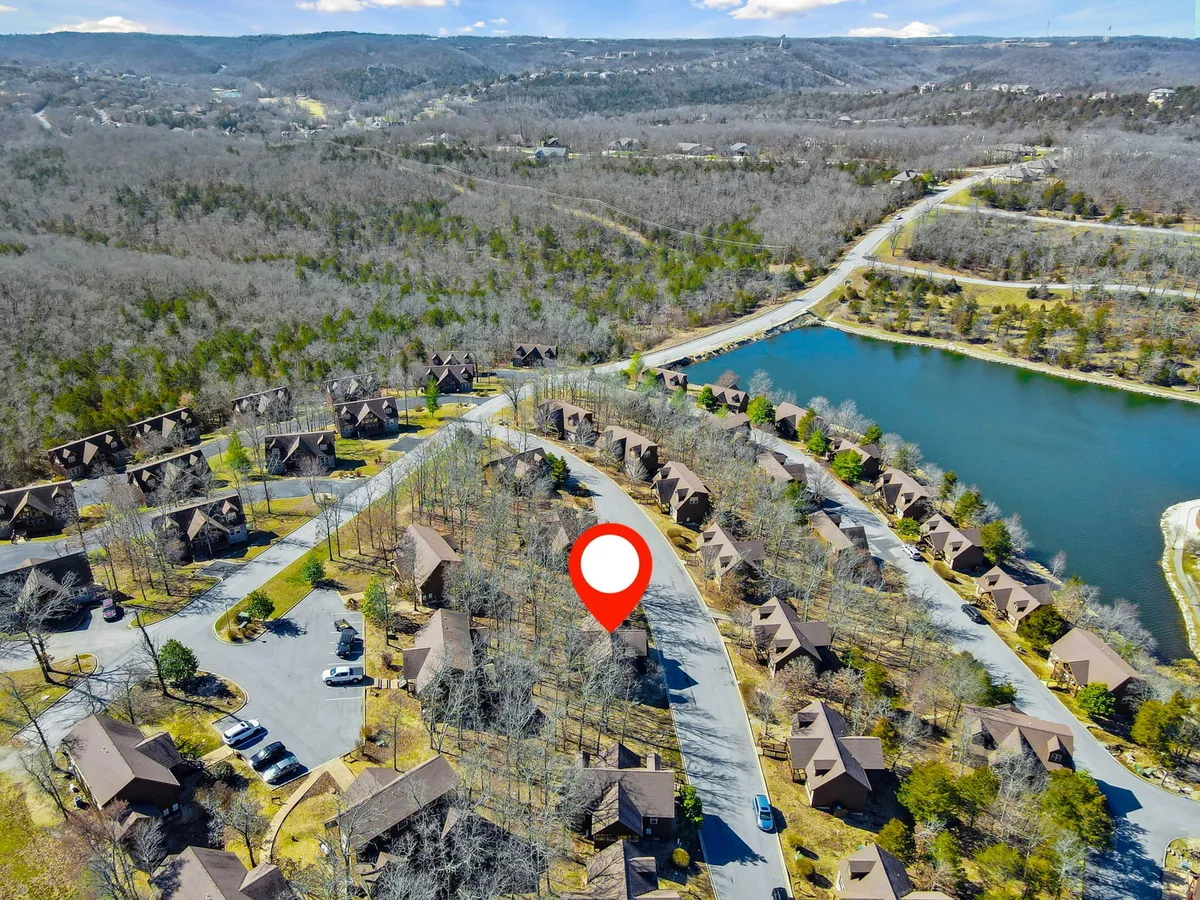 This image captures a tranquil scene featuring a cluster of cozy cabins nestled beside a serene lake, with a winding road leading through the area. The setting is surrounded by lush greenery, perfect for nature walks, fishing, and lakeside adventures with your pet.