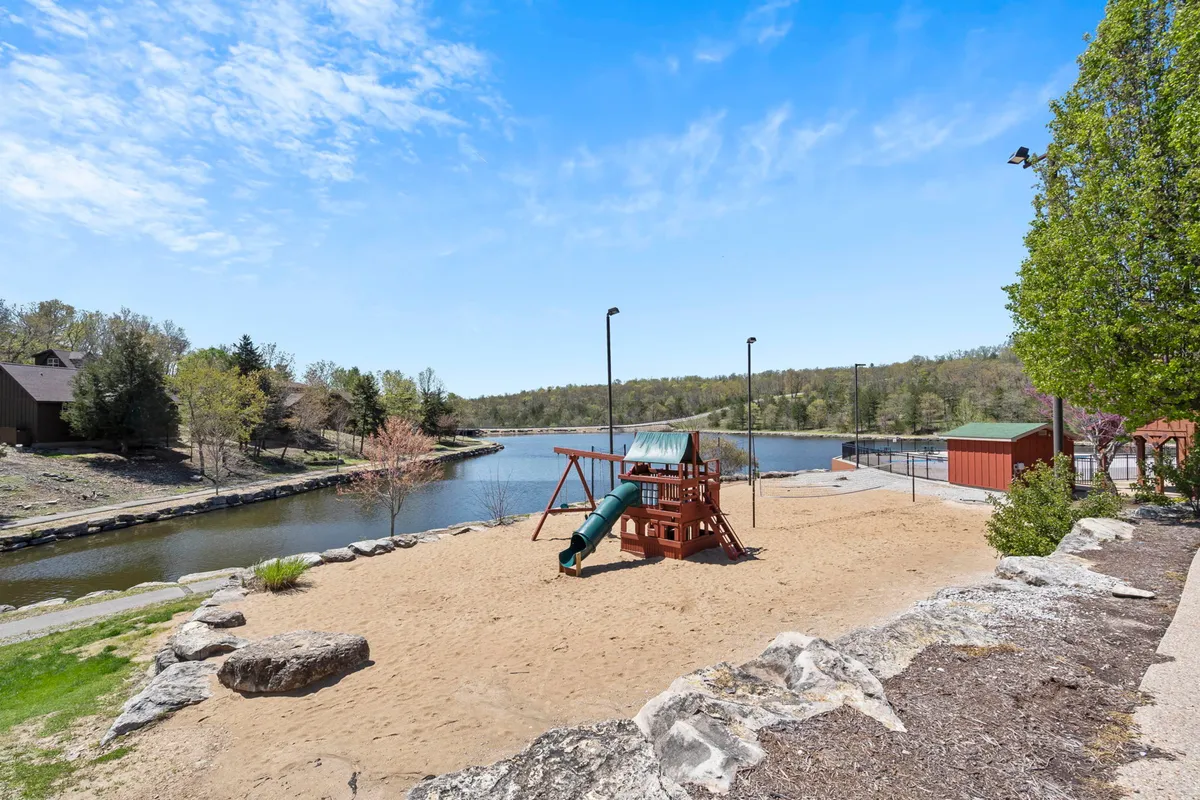 Overlooking a playful lakeside area, this image features a playground structure, a sandy area perfect for picnics, and a stunning view of the lake framed by trees. Families can be seen enjoying the outdoors, making it an ideal setting for inclusive, pet-friendly fun.