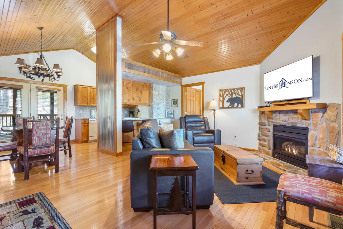 A cozy interior featuring a stone fireplace, wooden ceiling, and comfortable seating, with a dining area in the background. The space feels warm and welcoming, ideal for relaxing indoors during cooler months.