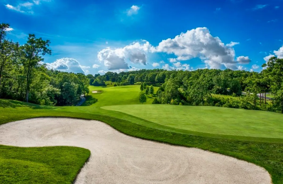 This image features an expansive view of the golf course, showcasing a sand trap set amidst lush greenery and under a vivid blue sky. The natural contours of the landscape and the well-manicured fairways are visible, providing a strong sense of the championship-level course and the tranquil mountain setting.