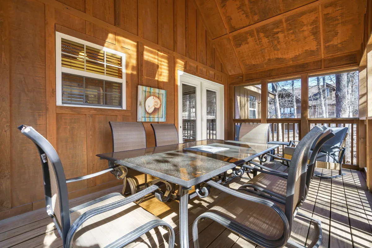 An interior scene with a glass-topped table and metal chairs set for dining, surrounded by wooden walls and decorative artwork, evoking a warm, inviting space for meals and relaxation.