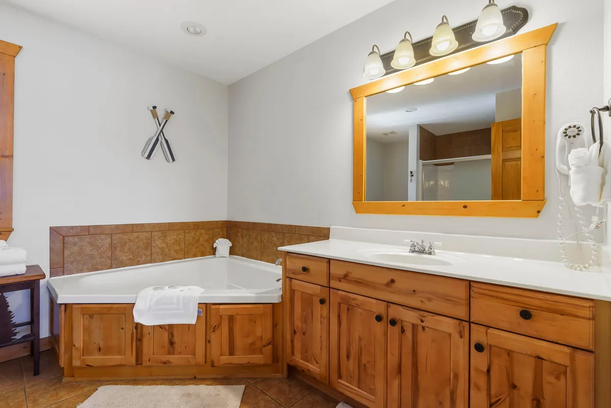 A spa-like bathroom scene with a luxurious bathtub, elegant vanity mirror, and wooden cabinetry. The room is softly lit, exuding a calming atmosphere ideal for relaxation and self-care.