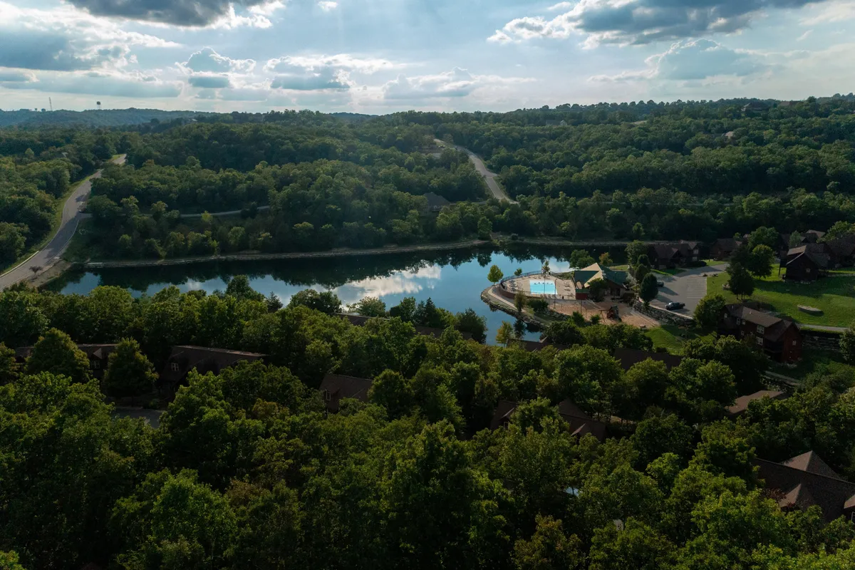 A sweeping view featuring a pristine swimming pool, reflective lake, lush greenery, and winding roadways. The landscape invites guests to relax by the pool, take a stroll, or enjoy the peaceful water views, capturing the spirit of relaxation and leisurely activities.