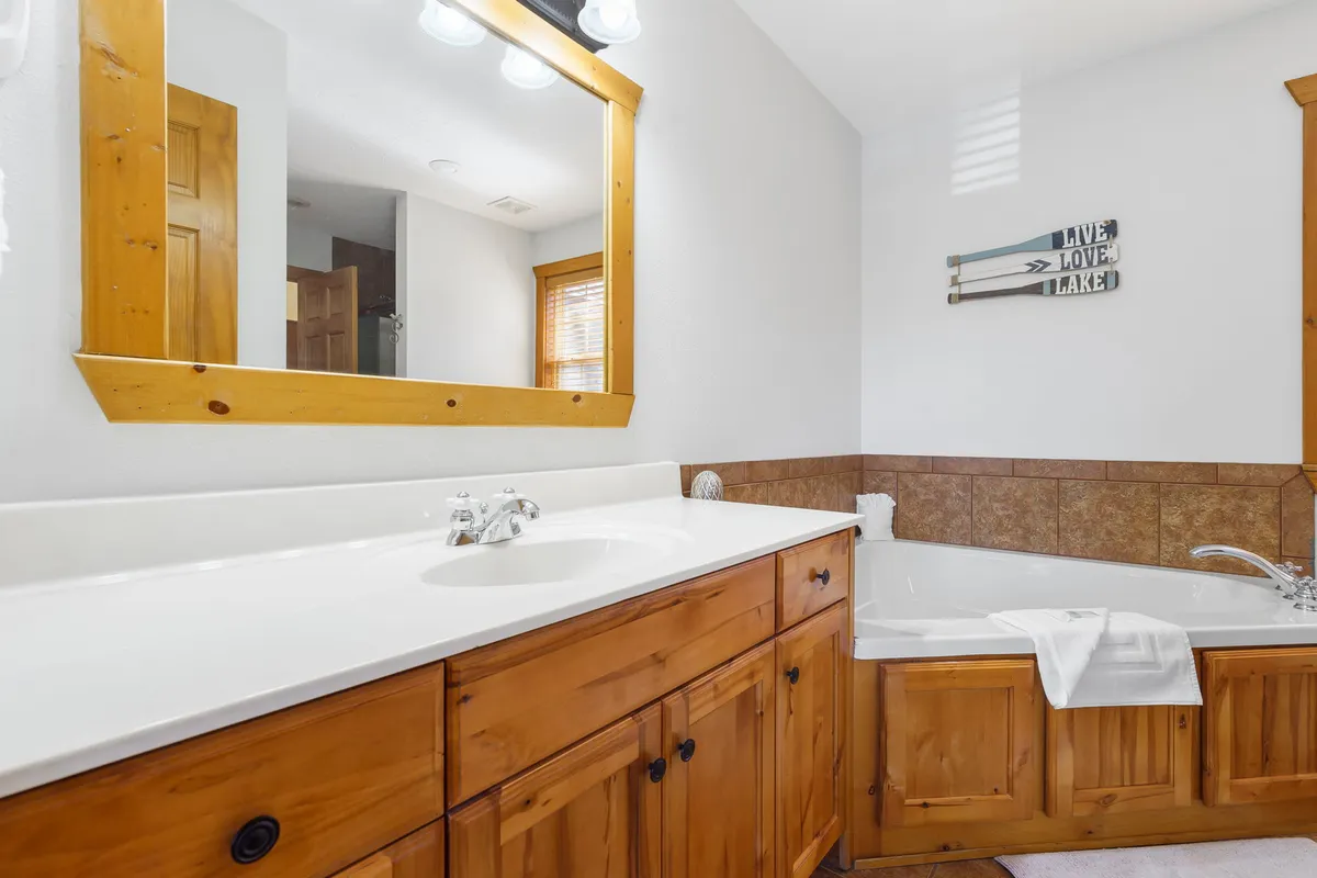 A calming bathroom with a large mirror above a wooden vanity, a spacious tub, and decorative touches. The ambiance is soothing, ideal for a relaxing soak or getting ready for the day.