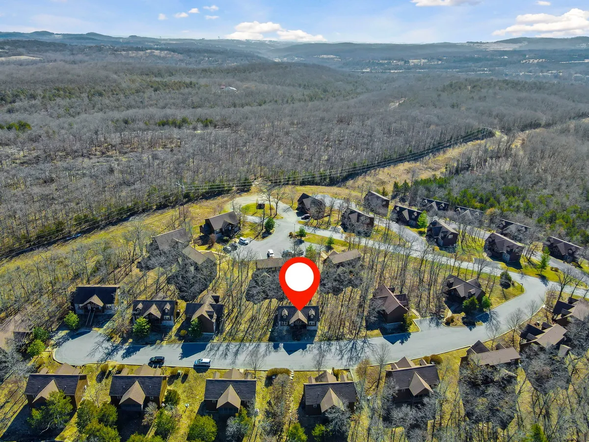 A tranquil circular road lined with clustered houses and surrounded by nature, with mature trees framing a peaceful neighborhood. The foliage hints at seasonal changes, offering glimpses of autumn colors and spring blossoms.